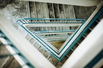俯瞰着一个三角形的楼梯井，楼梯井的扶手是青色的，台阶有些损坏